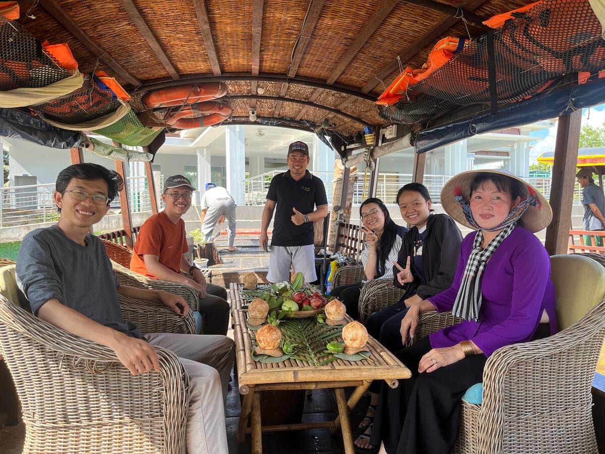 A group and their host at a table of coconuts and fruit on a boat in Bến Tre.